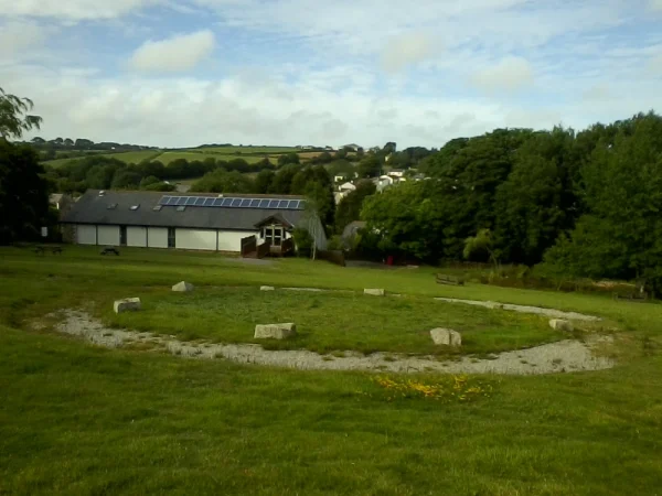View of a stone circle in the centre of Chacewater Millennium Green with Chacewater Village Hall and the village of Chacewater in the middle and far distance.